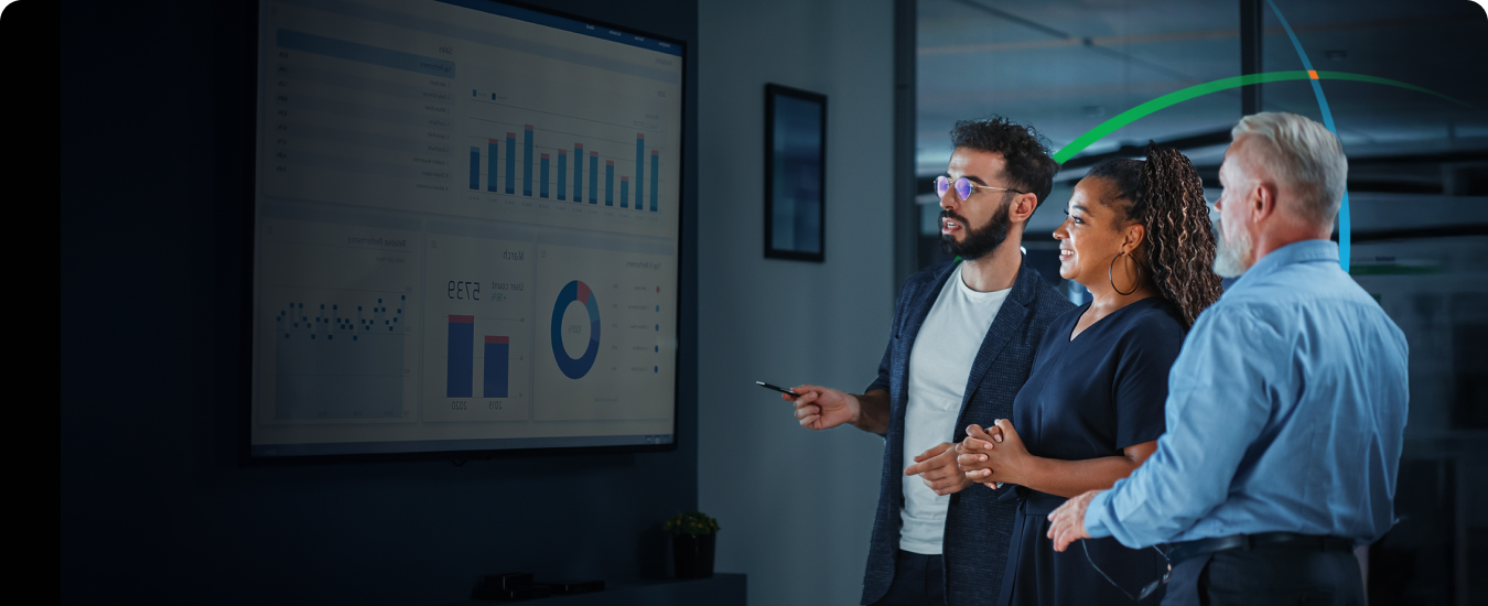 banner showing three business professionals having a discussion while looking at analytics dashboards on a large wall-mounted screen