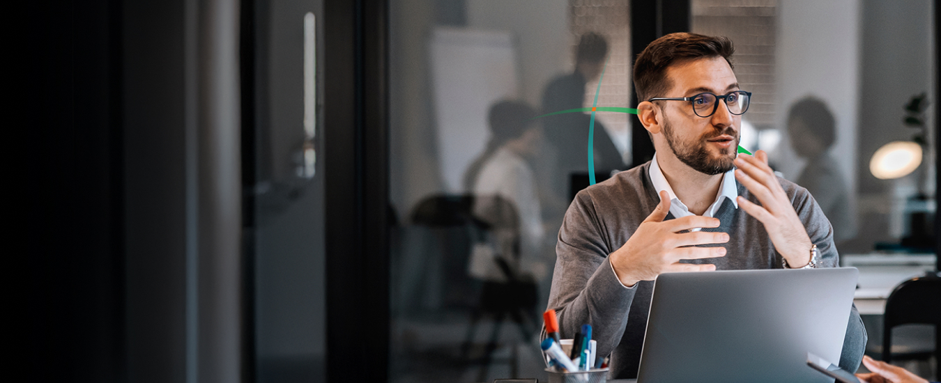 banner showing a man talking to another person while sitting in front of a laptop in a modern office setting