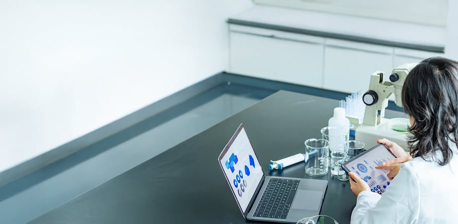 a medical professional in a lab looking at analytics dashboards on a tablet and a laptop