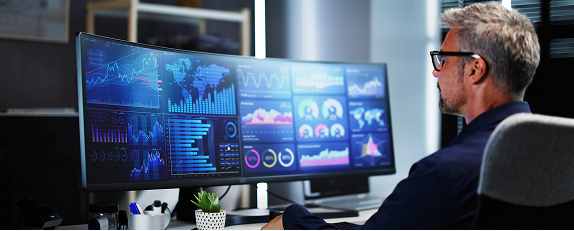 a man looking a wide computer screen displaying multiple analytics dashboards 
